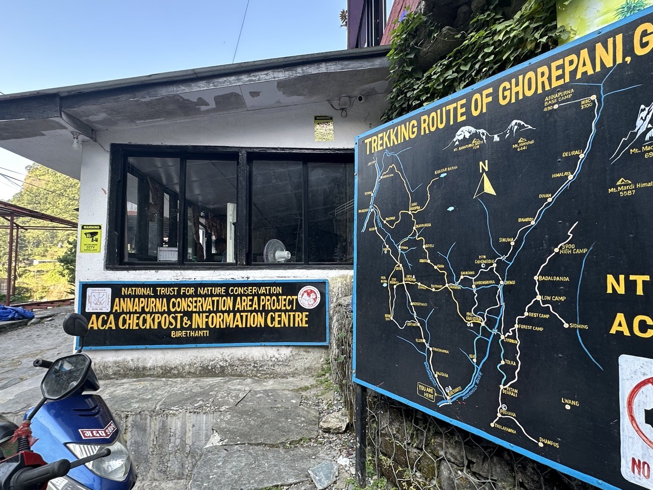 Birethanti trekking checkpoint showing permit entry point for the Poon Hill Trek, with trekkers registering at the entry counter, surrounded by riverside scenery and lush green hills of the Annapurna region.