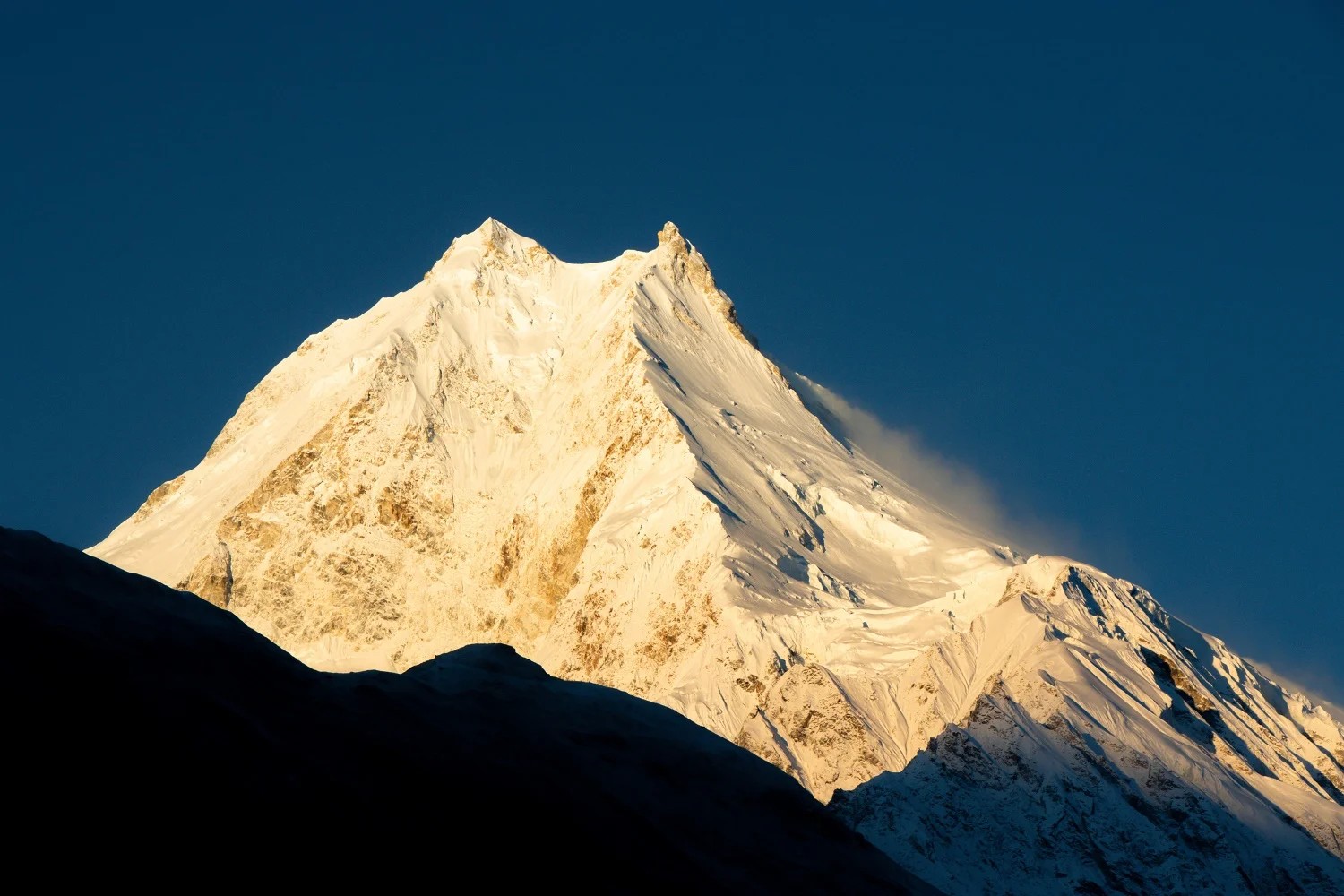 Golden sunrise light illuminating the majestic summit of Mount Manaslu, with snow-covered slopes glowing above the Himalayan landscape.