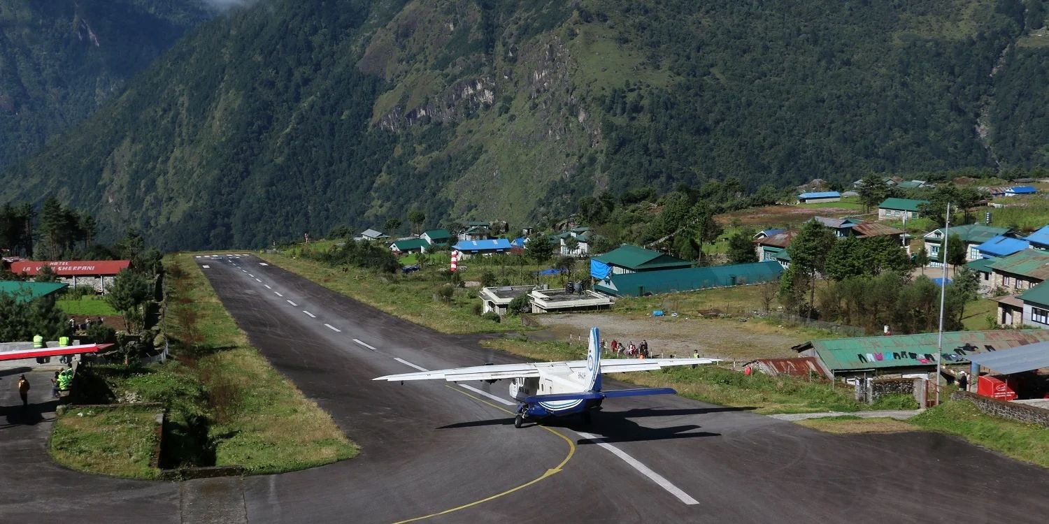 Lukla Airport runway surrounded by green hills and Himalayan mountains in the Everest region.