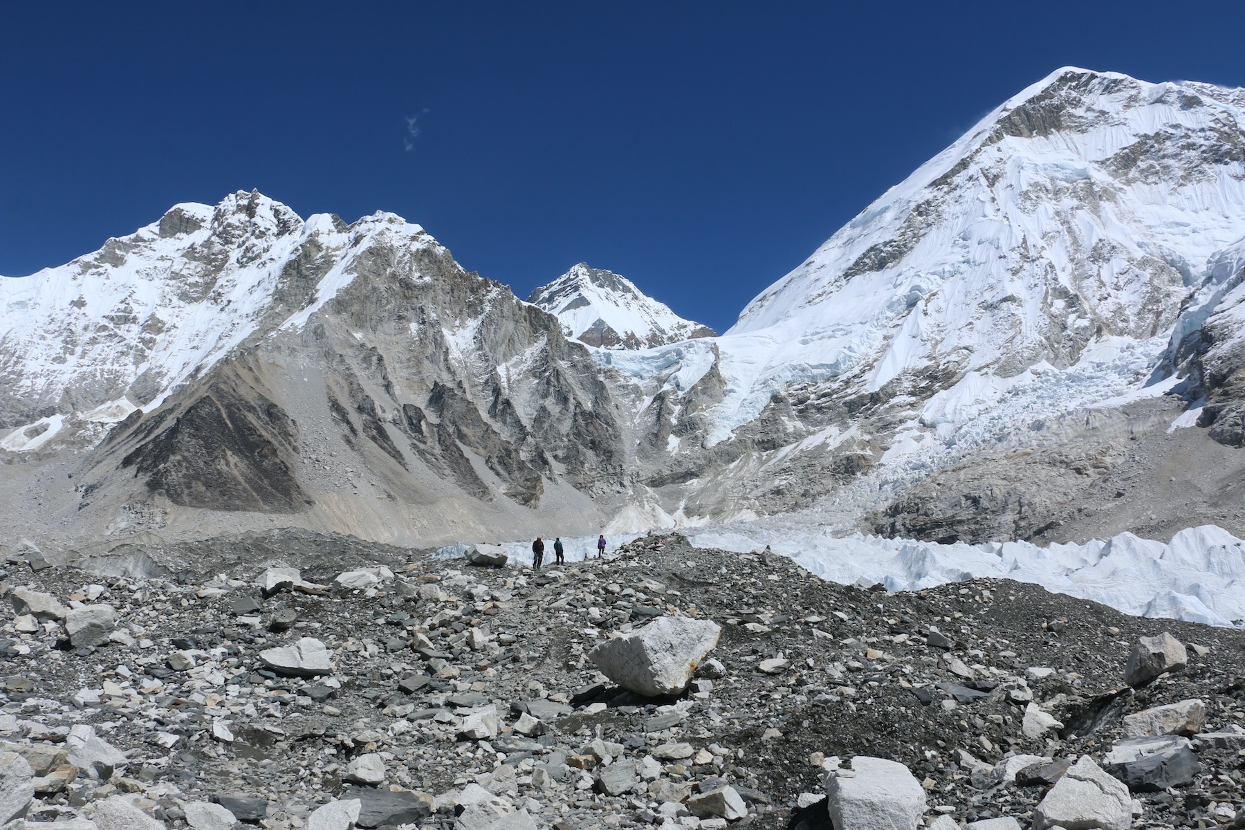 Trekkers ascending a Himalayan trail toward base camp viewpoint with snow-capped mountains, glaciers, and rugged alpine terrain in the background of Nepal.