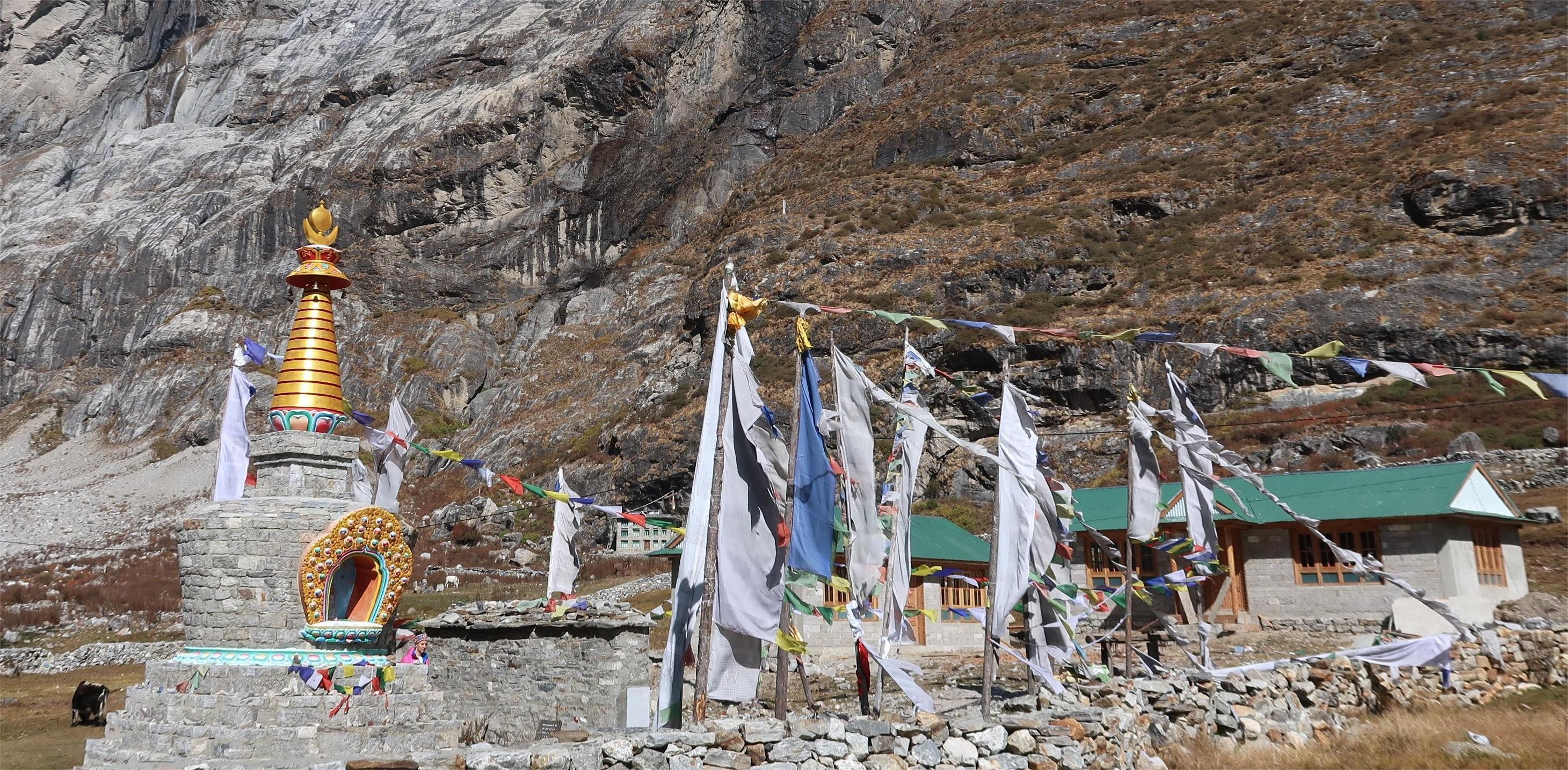 Buddhist stupa with colorful prayer flags fluttering in the wind in Langtang Valley, surrounded by Himalayan mountains, traditional stone paths, and peaceful mountain scenery.