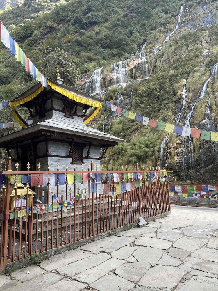 Baraha Temple surrounded by a beautiful cascading waterfall, lush green forest, moss-covered rocks, and serene Himalayan scenery on the Annapurna Base Camp Trek in Nepal.