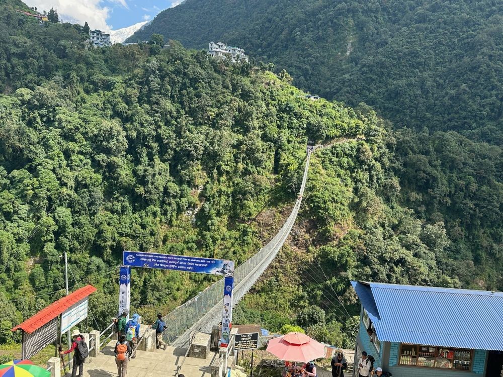Trekkers crossing the suspension bridge at Jhinu Danda, the exciting starting point of the Annapurna Base Camp Trek, surrounded by lush forests and the Modi Khola River.