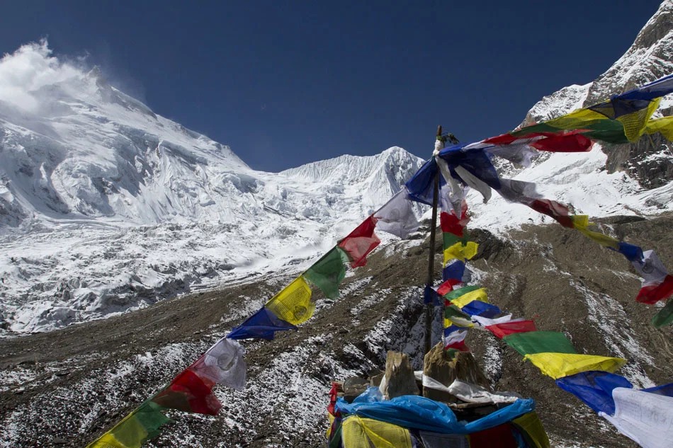 Colorful prayer flags overlooking the snow-covered Manaslu massif and rugged alpine landscape on the Manaslu Circuit Trek in Nepal.