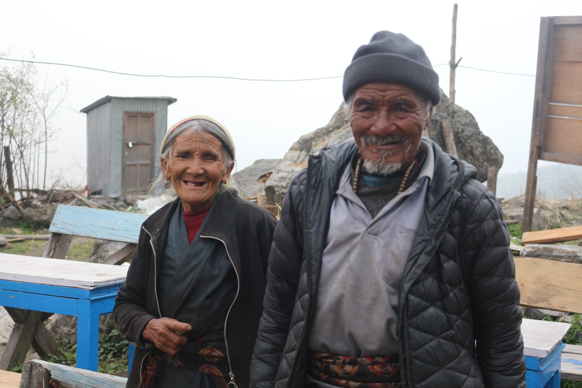 Local residents in traditional warm clothing in Langtang Valley with Himalayan mountains and stone houses in the background.