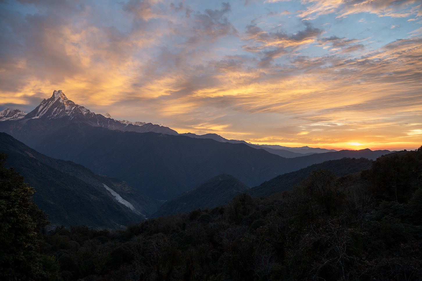 Sunrise view from Tadapani with soft orange clouds glowing in the morning sky, while the iconic Machhapuchhre (Fishtail Mountain) stands majestically above the Himalayan landscape