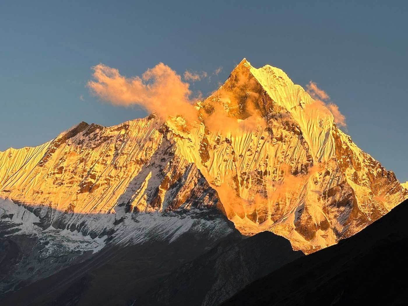 Machapuchare Base Camp in the Annapurna region with the iconic Fishtail Mountain (Machhapuchhre) silhouette glowing in golden hour light above alpine terrain and trekking tents.