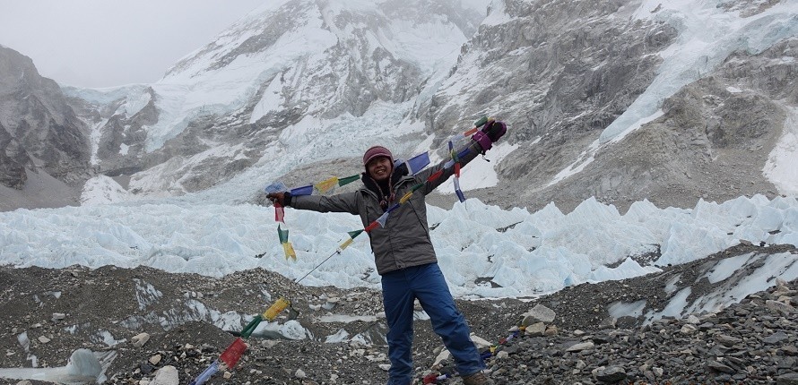 Everest Base Camp in September with colourful prayer flags, the Khumbu Glacier, and towering snow-covered Himalayan peaks beneath dramatic post-monsoon skies, as trekkers celebrate reaching the iconic destination