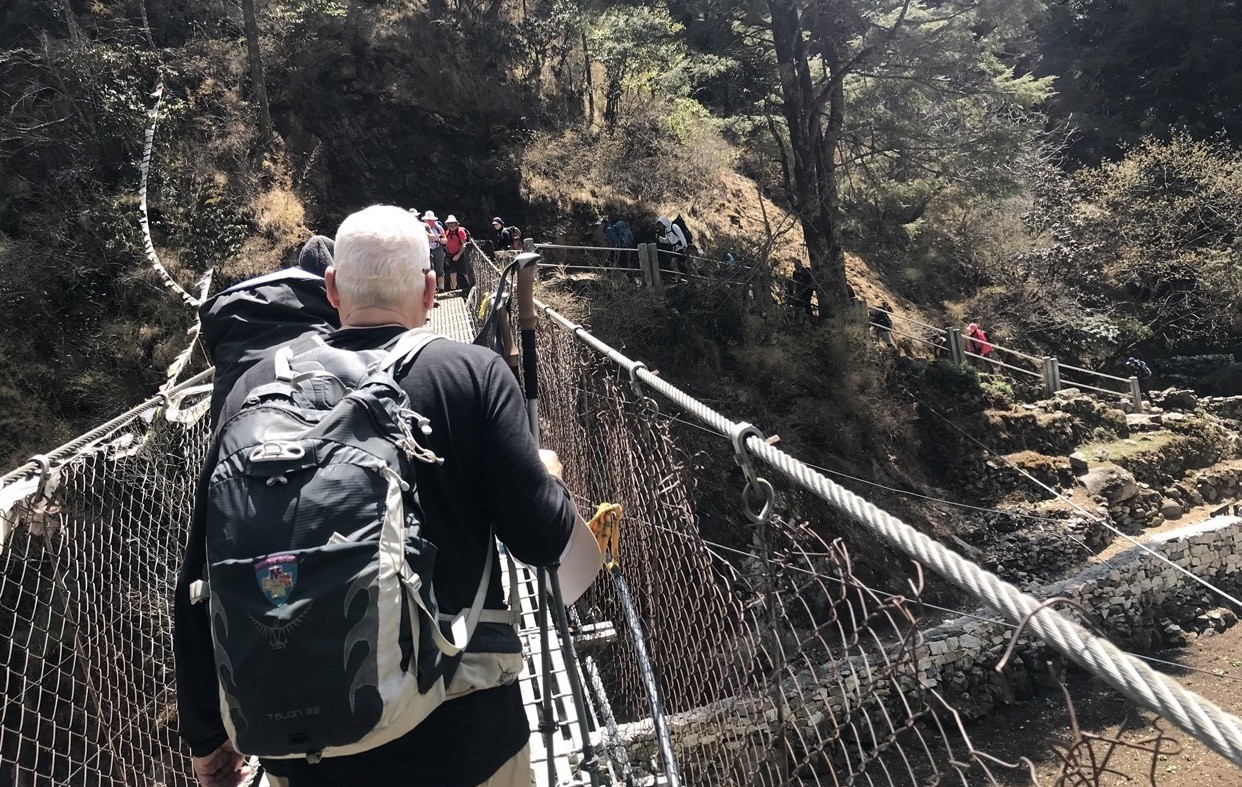 Busy Himalayan trekking trail in Nepal with groups of trekkers creating congestion on narrow paths, suspension bridges, and mountain routes during peak season.
