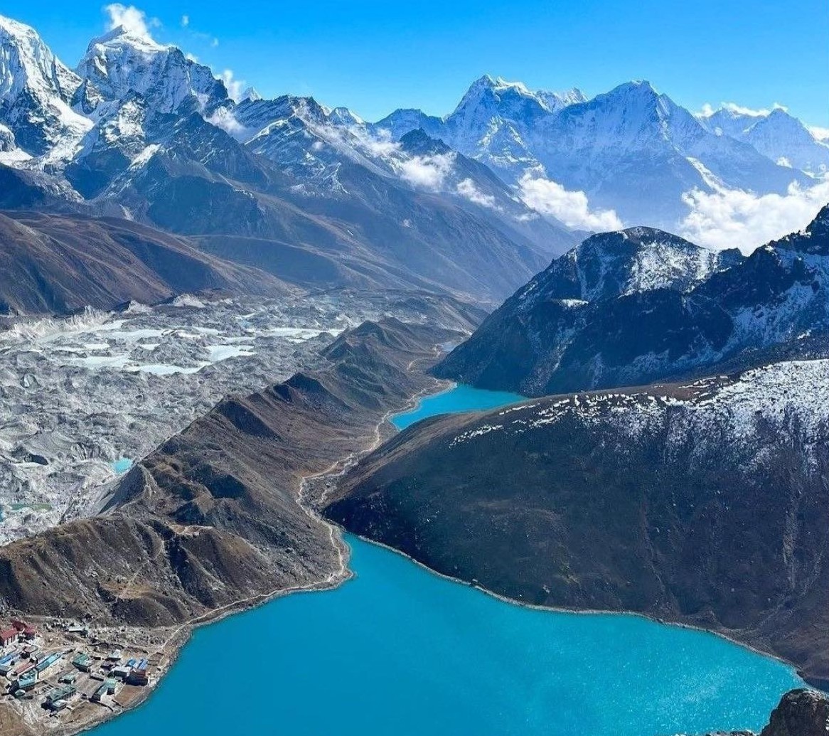 Crystal-clear view of Gokyo Lake in November with turquoise water, snow-covered Himalayan peaks, and blue autumn skies.