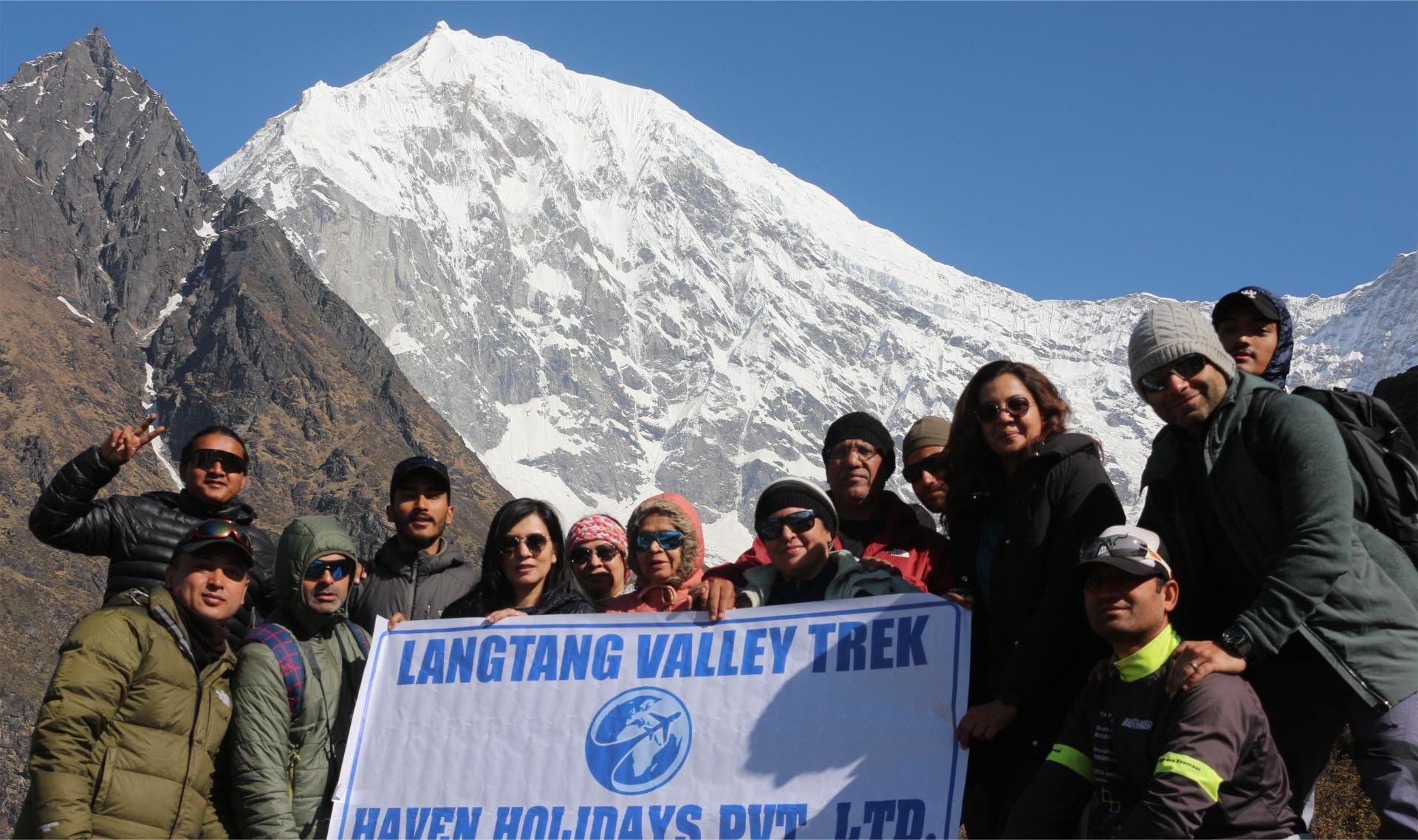 Haven Holidays trekking team group photo at the summit of Kyanjin Ri, celebrating together with panoramic views of the Langtang Himalayan range, glaciers, and alpine valleys.