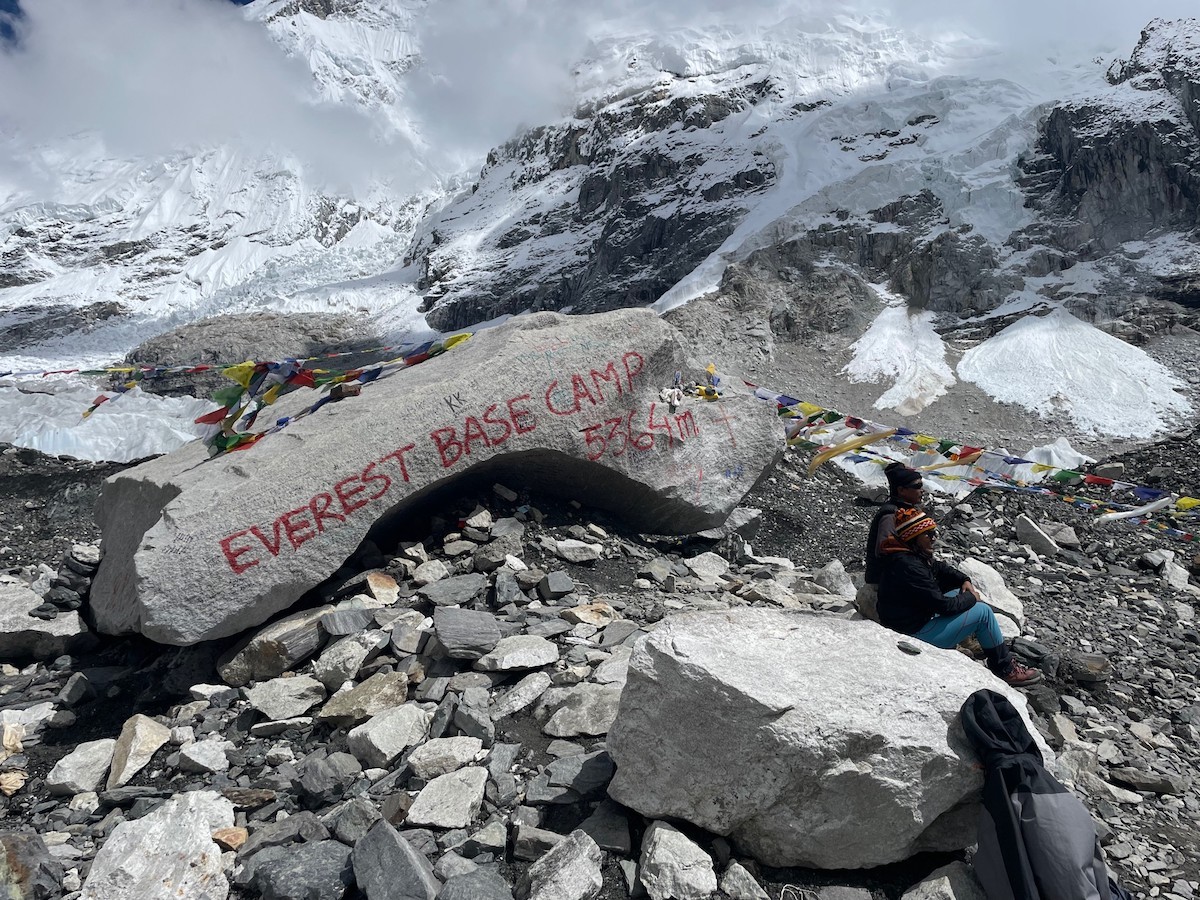Everest Base Camp with trekkers standing beside the famous stone marker, surrounded by the Khumbu Glacier, Khumbu Icefall, and spectacular views of Mount Everest, Nuptse, and the Himalayan peaks. 