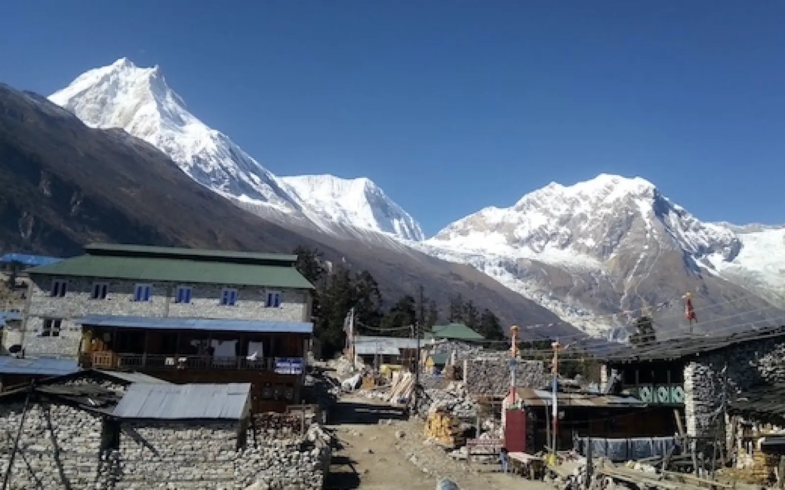 Syala village on the Manaslu Circuit Trek with traditional stone houses, colorful prayer flags, lush alpine meadows, and stunning views of Mount Manaslu and surrounding Himalayan peaks.