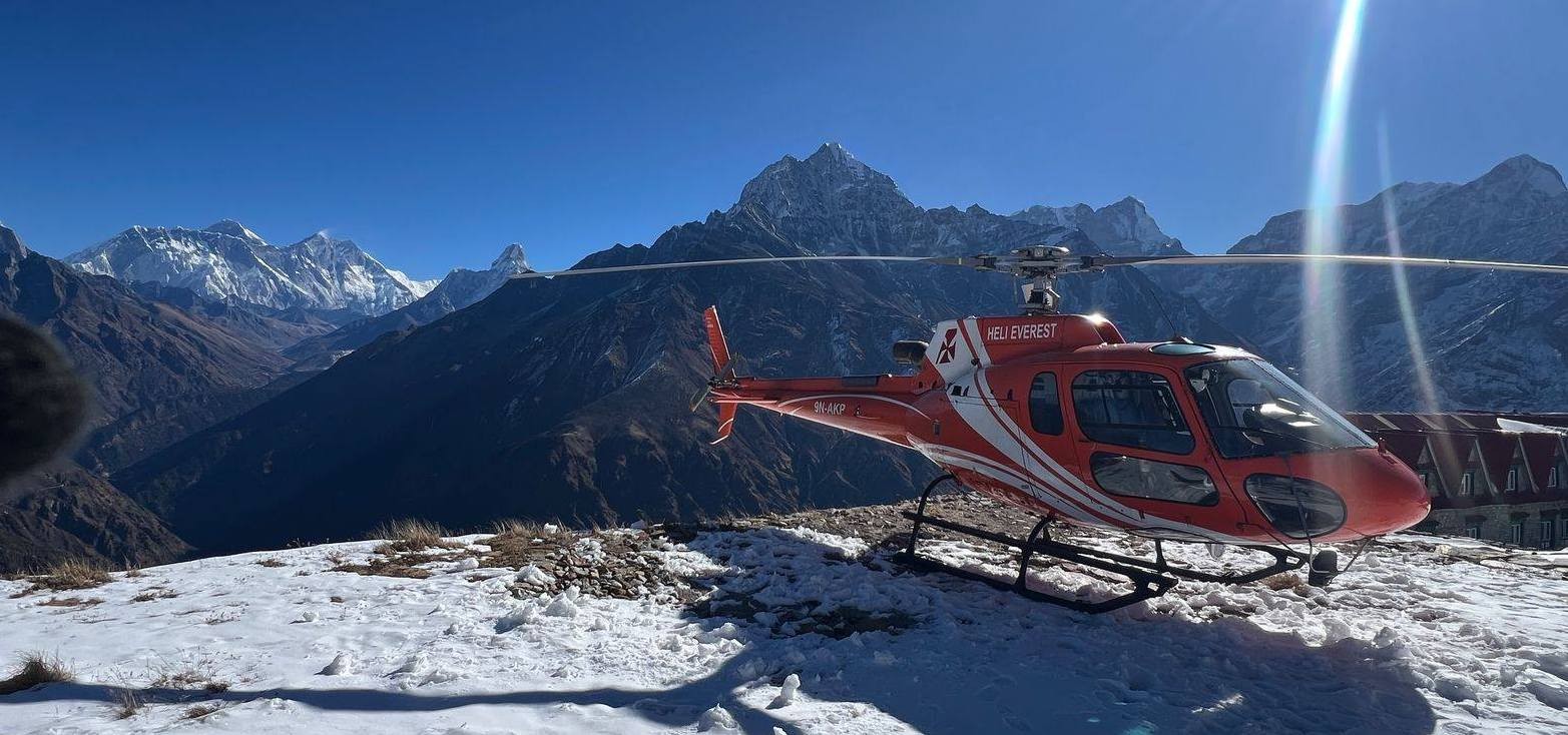 Helicopter picking up trekkers near Gorak Shep in the Everest region with Mount Everest and Himalayan peaks in the background.