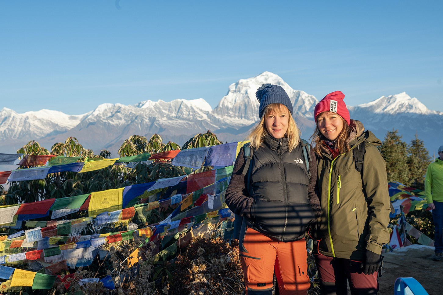 Poon Hill sunrise with prayer flags and trekkers overlooking the Dhaulagiri mountain range.