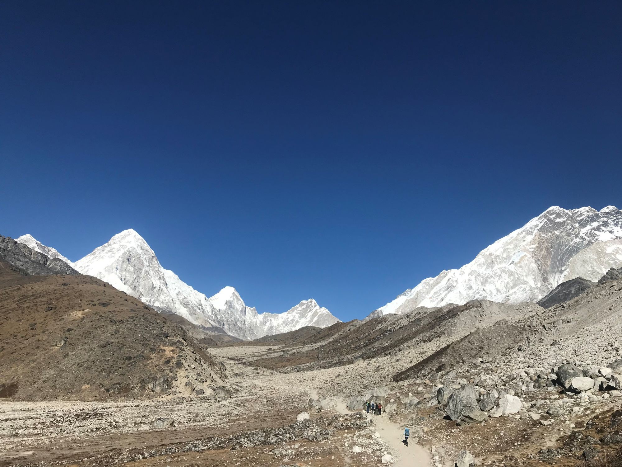 Trekkers hiking on the trail to Lobuche through the rugged alpine landscape with snow-covered Himalayan peaks in the Everest region.