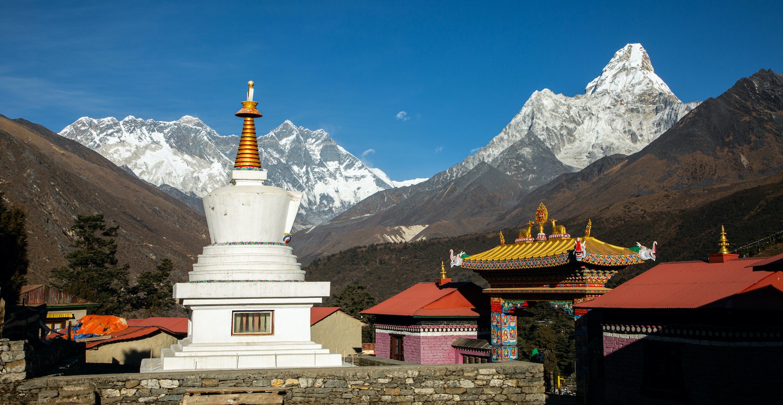 Tengboche Monastery set on a mountain ridge in the Everest region, with panoramic views of snow-capped Himalayan peaks including Ama Dablam under a clear alpine sky.