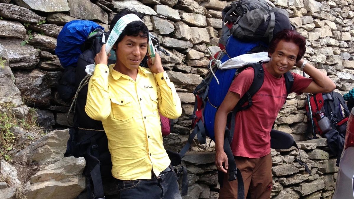 Everest Base Camp Trek porter carrying trekking gear along a rugged mountain trail with towering Himalayan peaks in the background.