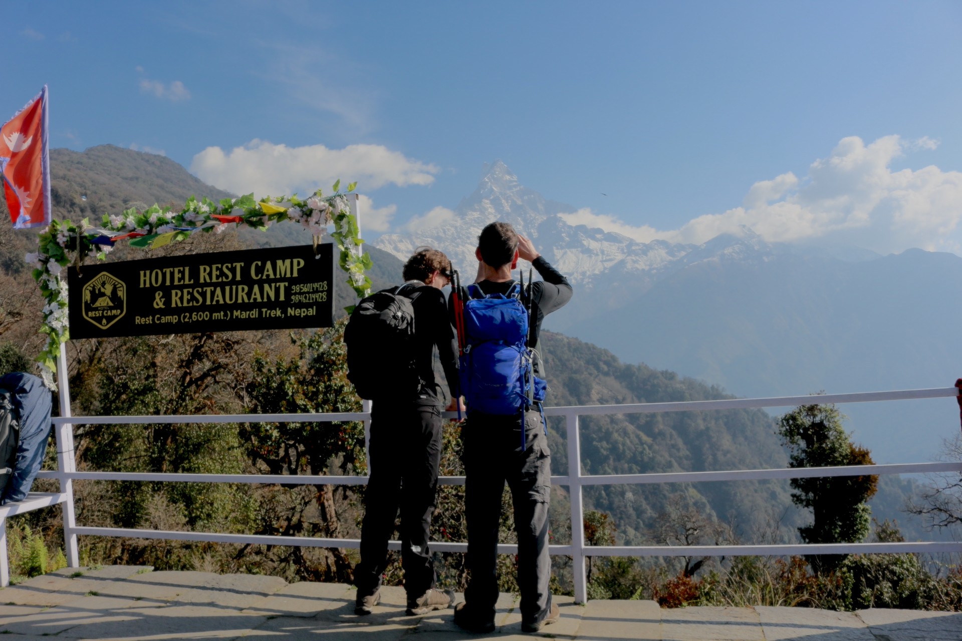 Trekkers enjoying panoramic views from Rest Camp on the Mardi Himal Trek, with Machhapuchhre (Fishtail Mountain) rising above lush hills under a clear blue October sky in Nepal.