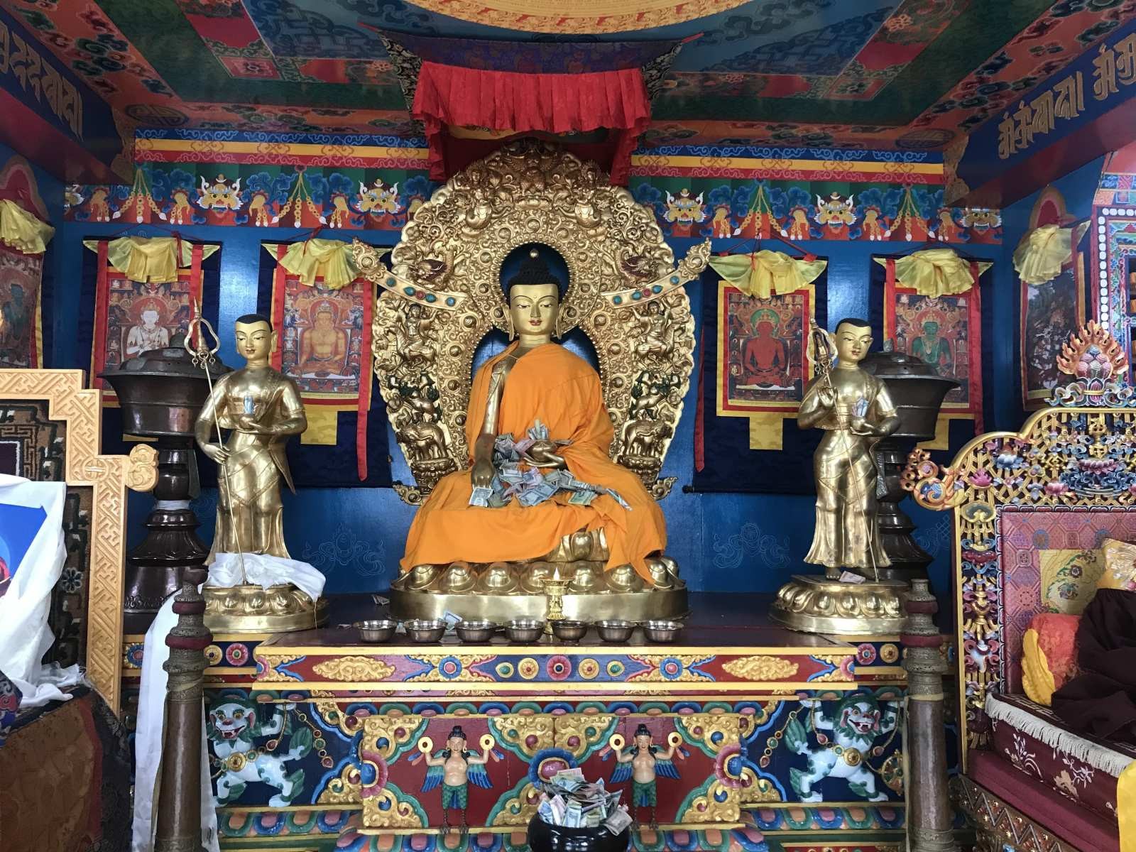 Golden Buddha statue inside a traditional Sherpa monastery on the Everest Base Camp Trek, surrounded by colorful prayer flags, intricate murals, butter lamps, and sacred Buddhist decorations.