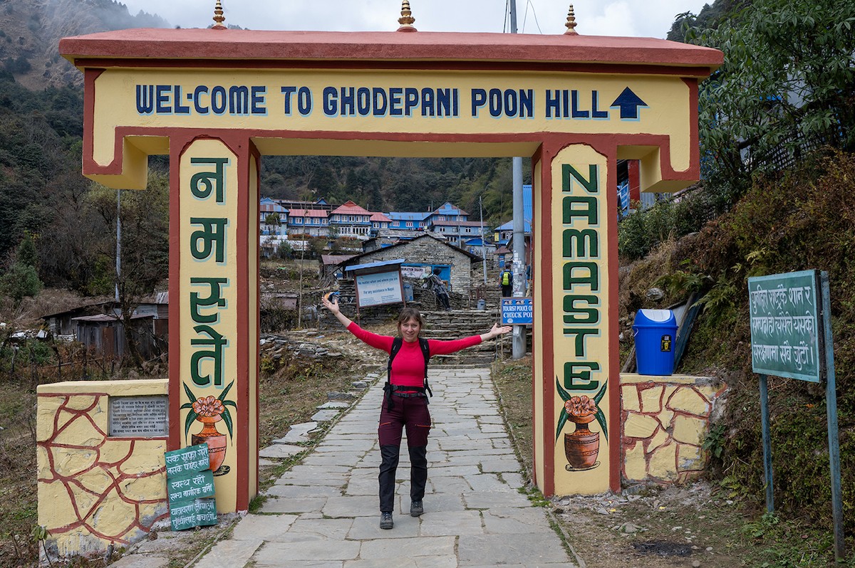 Happy trekkers posing at the Ghorepani Gate, surrounded by colorful village scenery, rhododendron forests, and the beautiful Himalayan landscape of the Annapurna region.