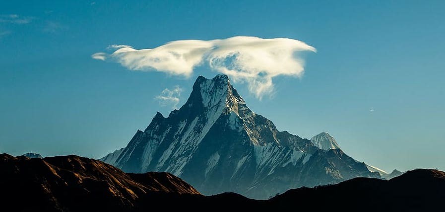 "Machhapuchhre (Fishtail Mountain) in September, Nepal, crowned by a lenticular cloud above its snow-covered summit under clear post-monsoon Himalayan skies." 