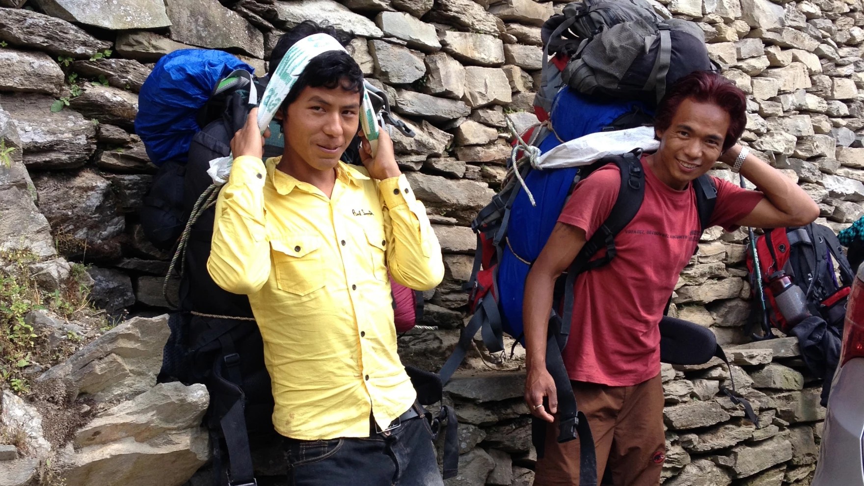 Everest Base Camp Trek porter carrying trekking gear along a rugged mountain trail with towering Himalayan peaks in the background.
