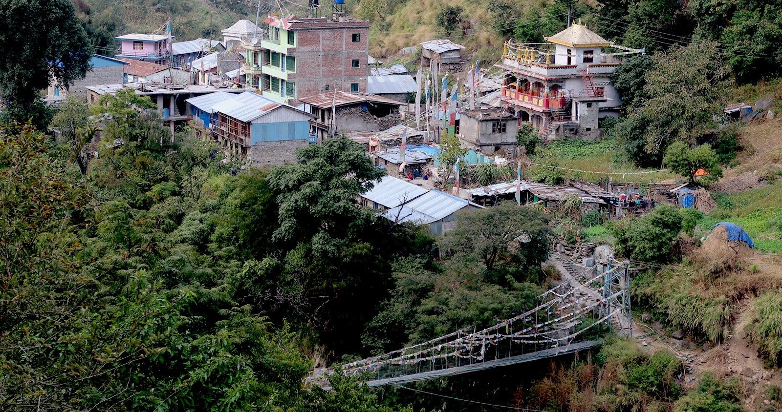 Syabrubesi village in October with lush green hills, the Bhote Koshi River, traditional houses, and clear blue skies at the gateway to the Langtang Valley Trek in Nepal.