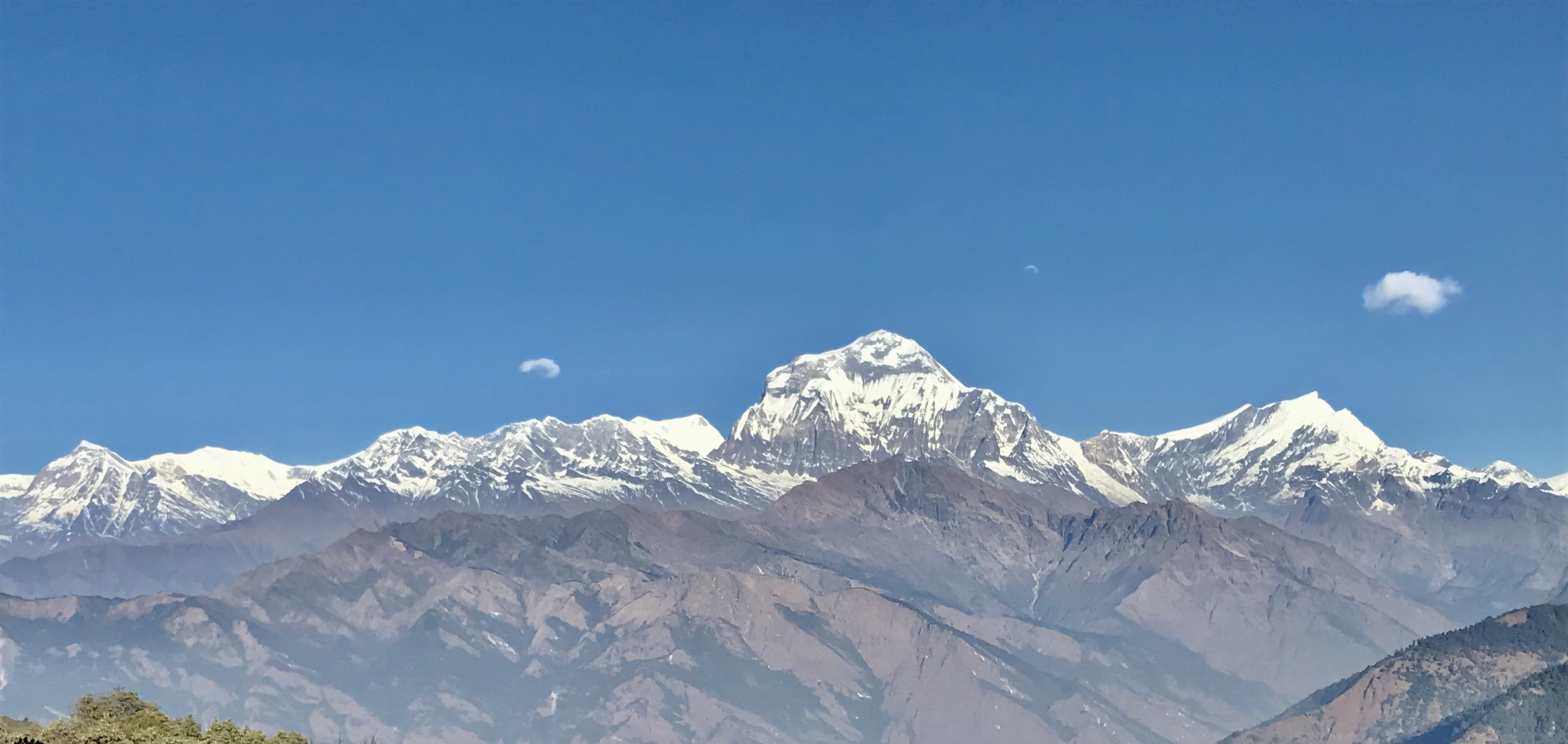 "Autumn panorama from Poon Hill featuring the snow-covered Annapurna and Dhaulagiri mountain ranges beneath a crystal-clear blue sky in Nepal's Annapurna Conservation Area.