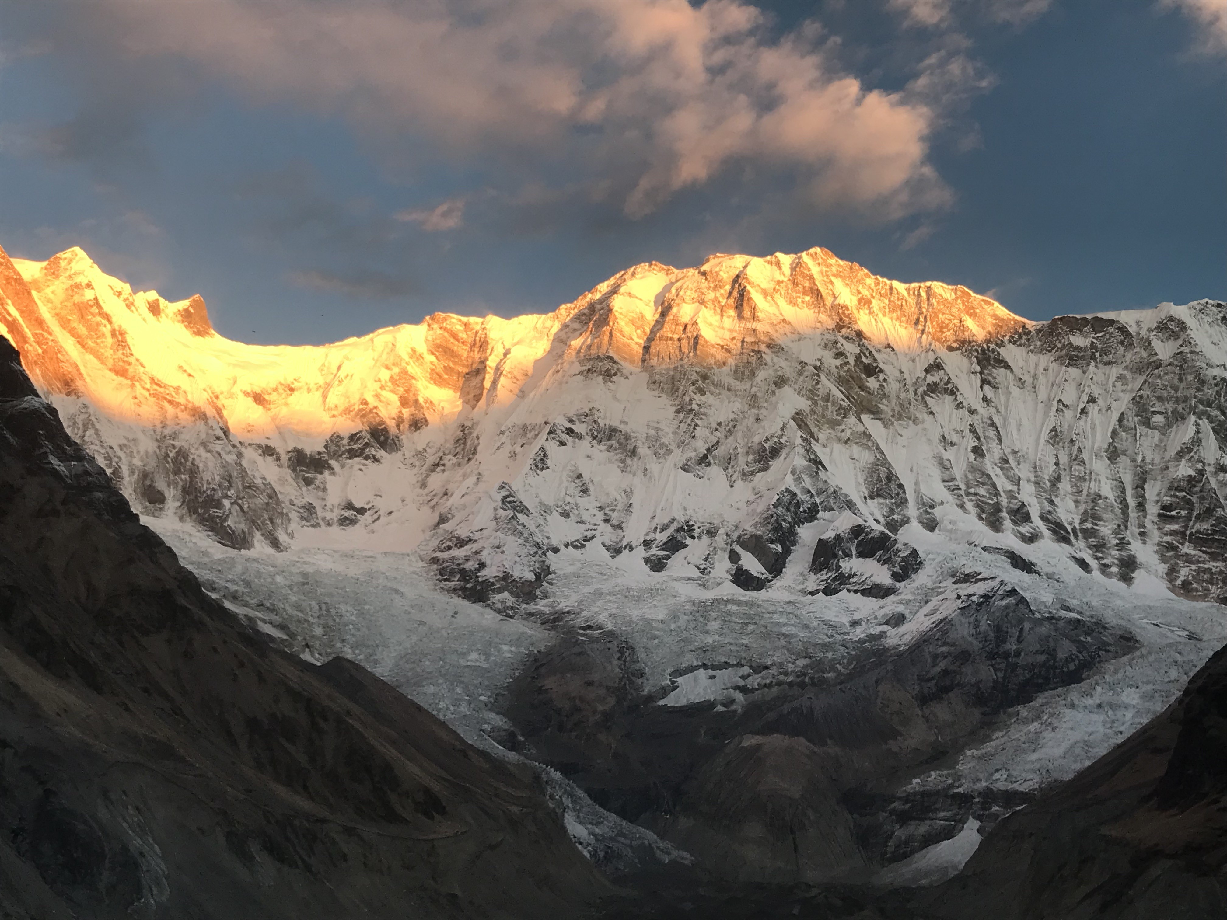 Golden sunrise illuminating Annapurna I with warm orange and golden light, creating a spectacular glow across the snow-covered Himalayan peak and surrounding mountains