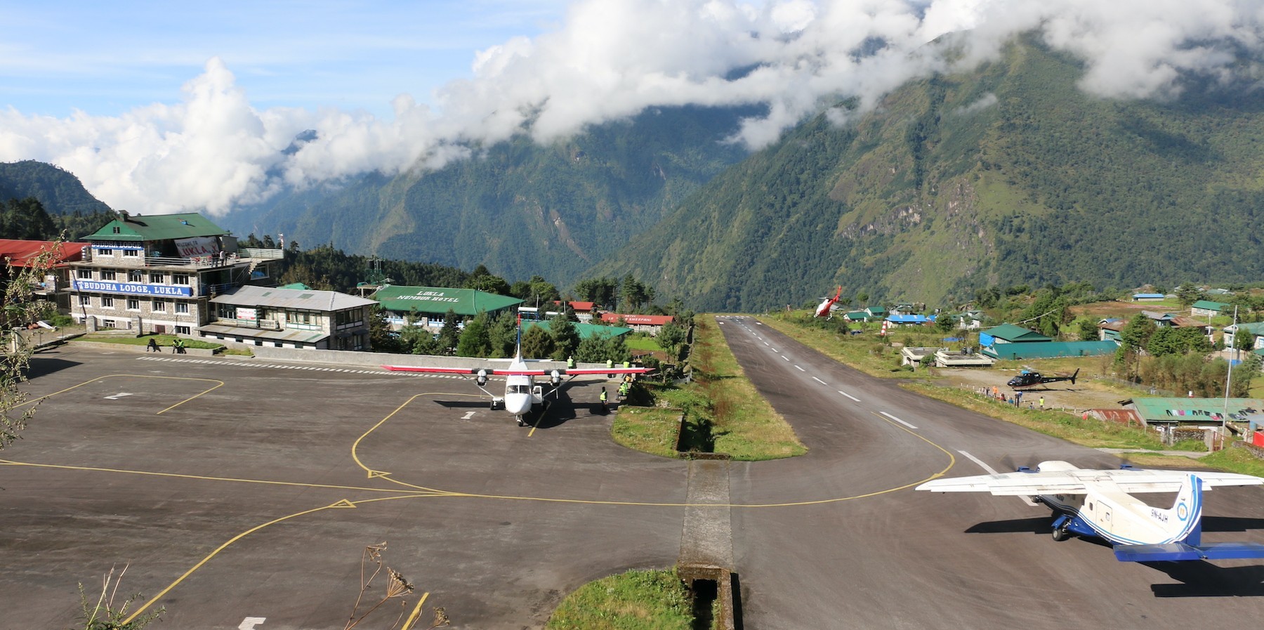 A small aircraft parked on the runway at Lukla Airport, surrounded by dramatic Himalayan mountains, marking the gateway to the Everest Base Camp Trek.