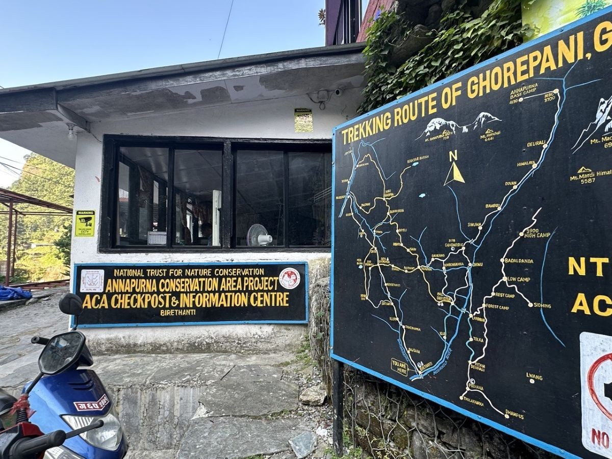 Birethanti trekking checkpoint showing permit entry point for the Poon Hill Trek, with trekkers registering at the entry counter, surrounded by riverside scenery and lush green hills of the Annapurna region.