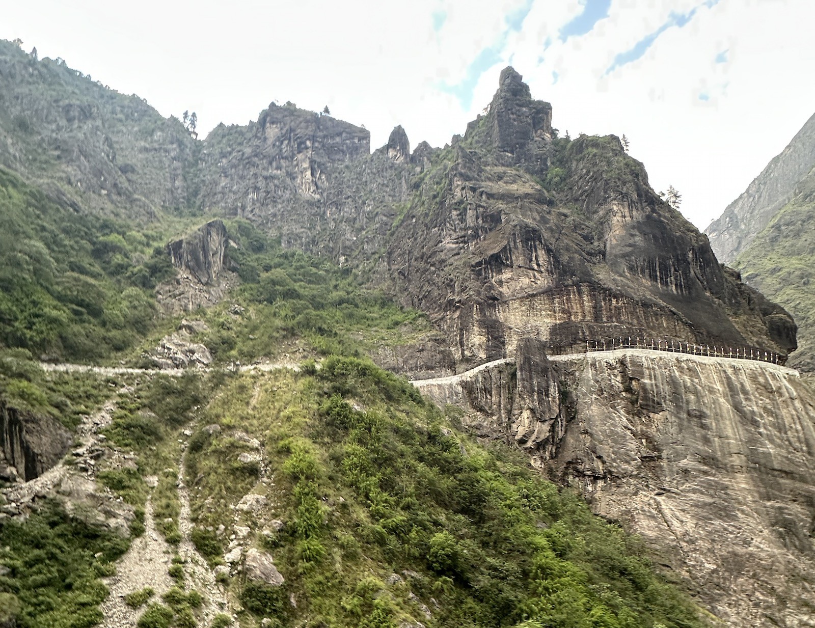 Rugged mountain road leading to Manang along the Annapurna Circuit Trek, showing jeep tracks carved into rocky cliffs, river valleys, and towering Himalayan peaks in the background.