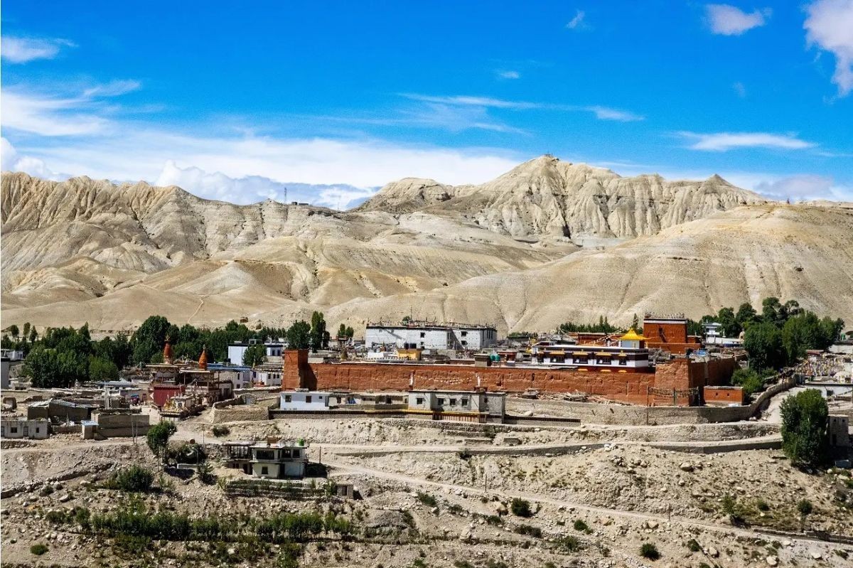Trekkers walking through the rugged Upper Mustang landscape with dramatic cliffs, barren valleys, and traditional mountain villages.