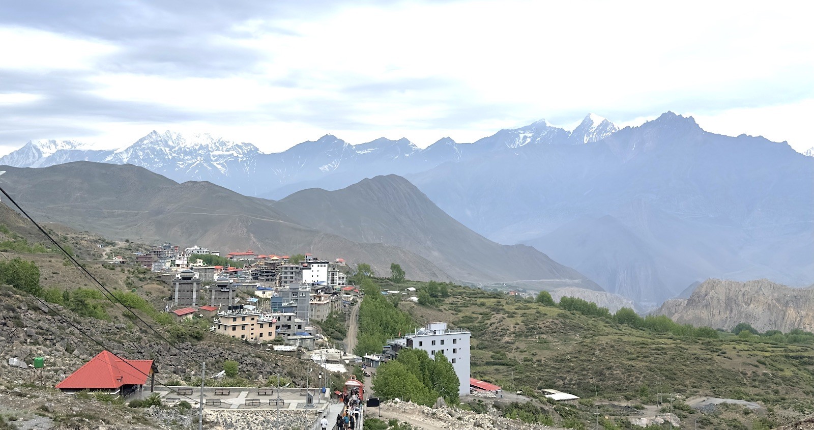 Scenic view of Muktinath Temple settlement in the Mustang Valley, featuring traditional stone buildings, prayer flags, dry Himalayan landscape, and snow-capped mountain ranges in the background.