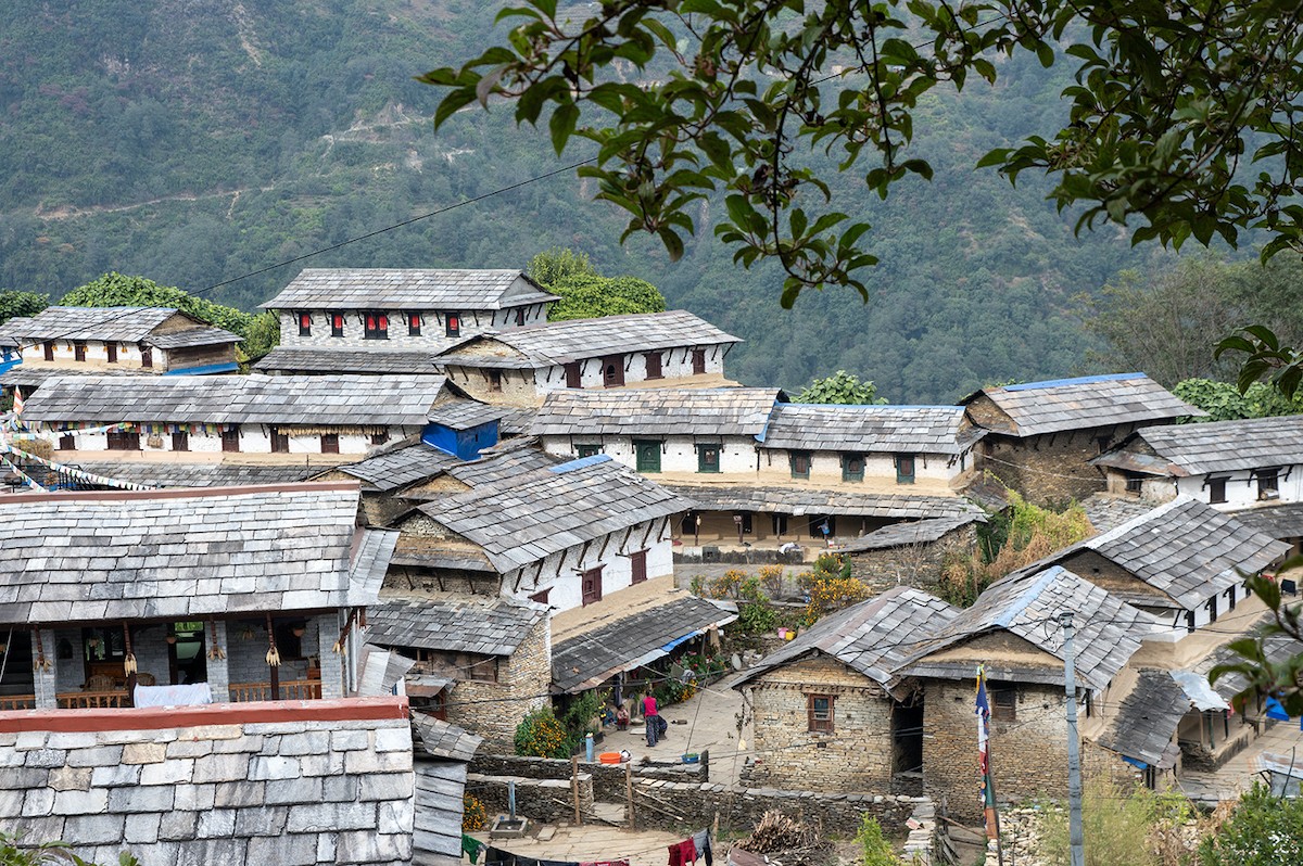 Ghandruk village traditional stone-paved alleys, authentic Gurung stone houses, local villagers in traditional attire, prayer flags, and breathtaking views of Annapurna South and Machhapuchhre.