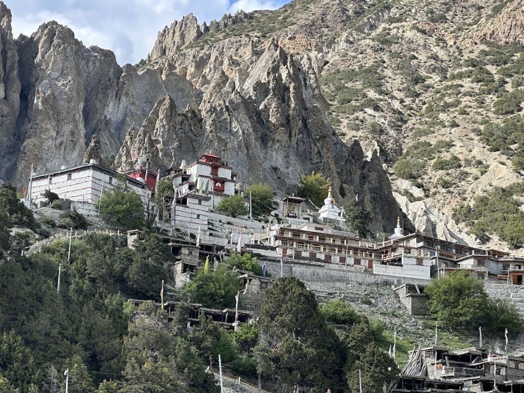 Traditional Braga Village with ancient stone houses, Braga Monastery, colorful prayer flags, and panoramic views of the Annapurna Himalayas near Manang on the Annapurna Circuit Trek in Nepal.