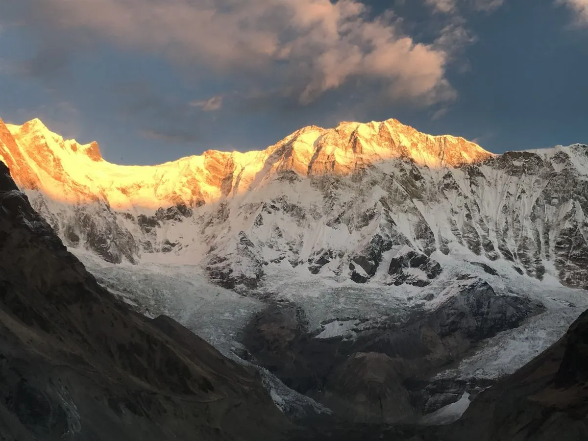 Golden sunrise illuminating Annapurna I with warm orange and golden light, creating a spectacular glow across the snow-covered Himalayan peak and surrounding mountains