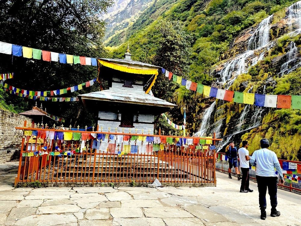 Baraha Temple beside the Modi Khola Gorge on the Annapurna Base Camp Trek, surrounded by lush forest, a flowing waterfall, and scenic Himalayan landscapes.