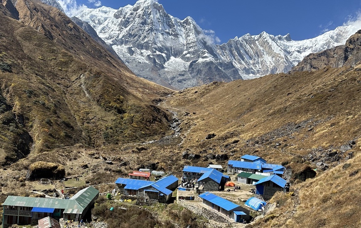 Machhapuchhre Base Camp (MBC) with blue-roofed teahouses surrounded by towering snow-covered peaks, including Machhapuchhre (Fishtail) and Annapurna South, on the Annapurna Base Camp Trek in Nepal.