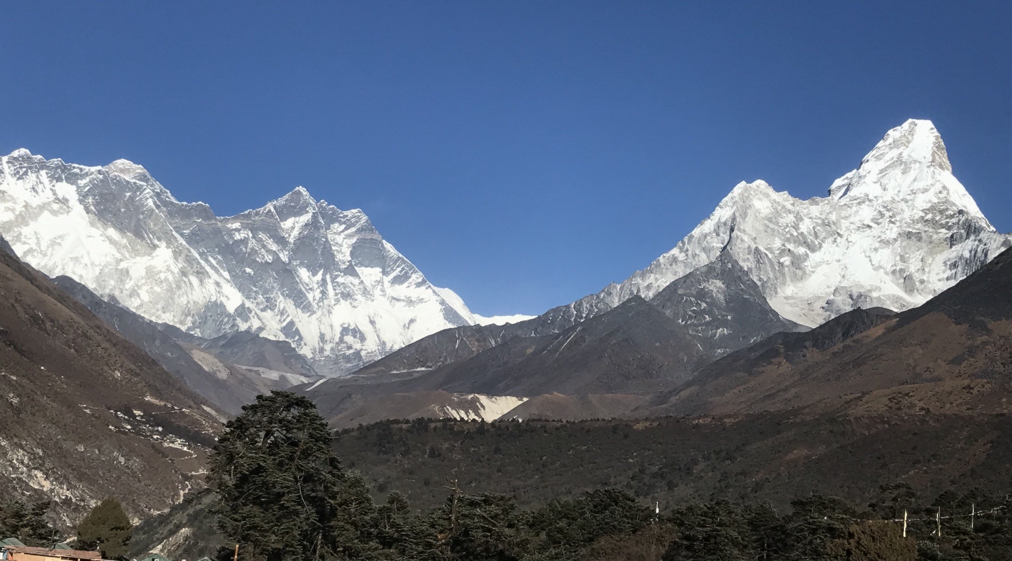 Panoramic view of Mount Everest, Lhotse, Nuptse, and Ama Dablam under a crystal-clear blue sky, with alpine forests and rugged Himalayan valleys on the Everest Base Camp Trek.