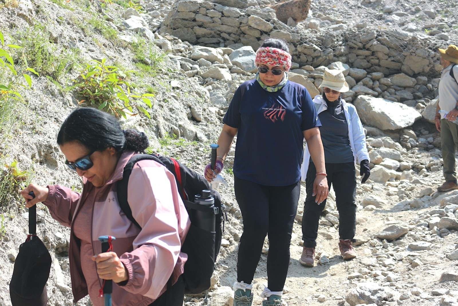  Trekkers wearing sturdy waterproof trekking boots while crossing rocky scree slopes and mountain streams on the Langtang Valley Trek, surrounded by rugged Himalayan terrain and snow-capped peaks.