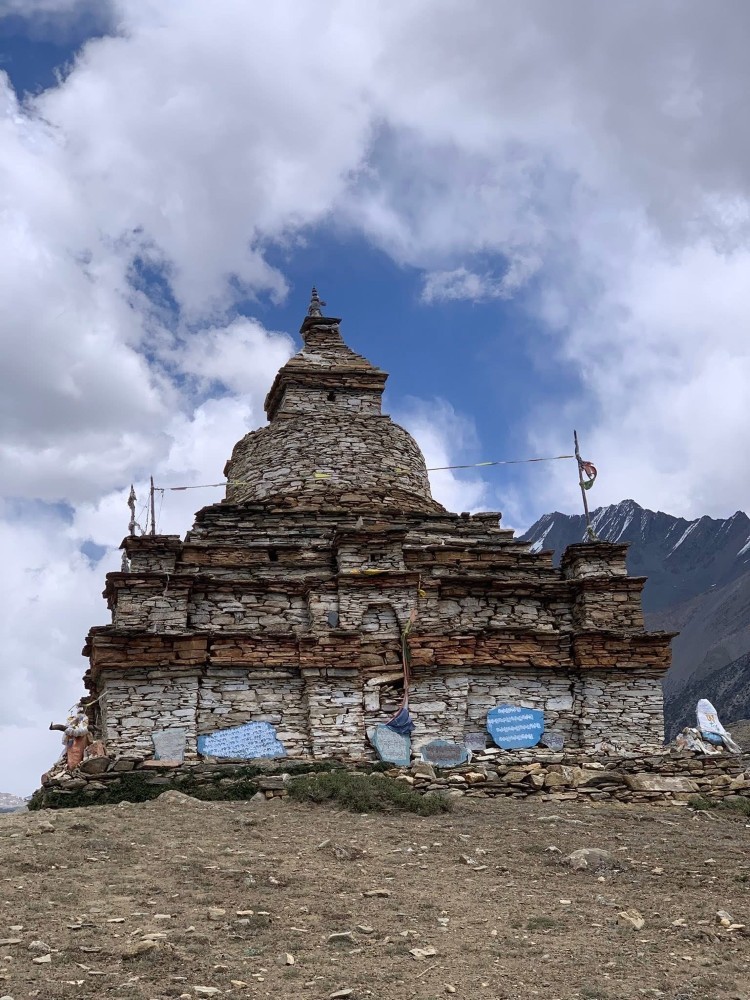 Ancient stone stupa in the Himalayan region of Nepal, built from stacked local rocks and surrounded by rugged mountain landscapes and prayer flags.
