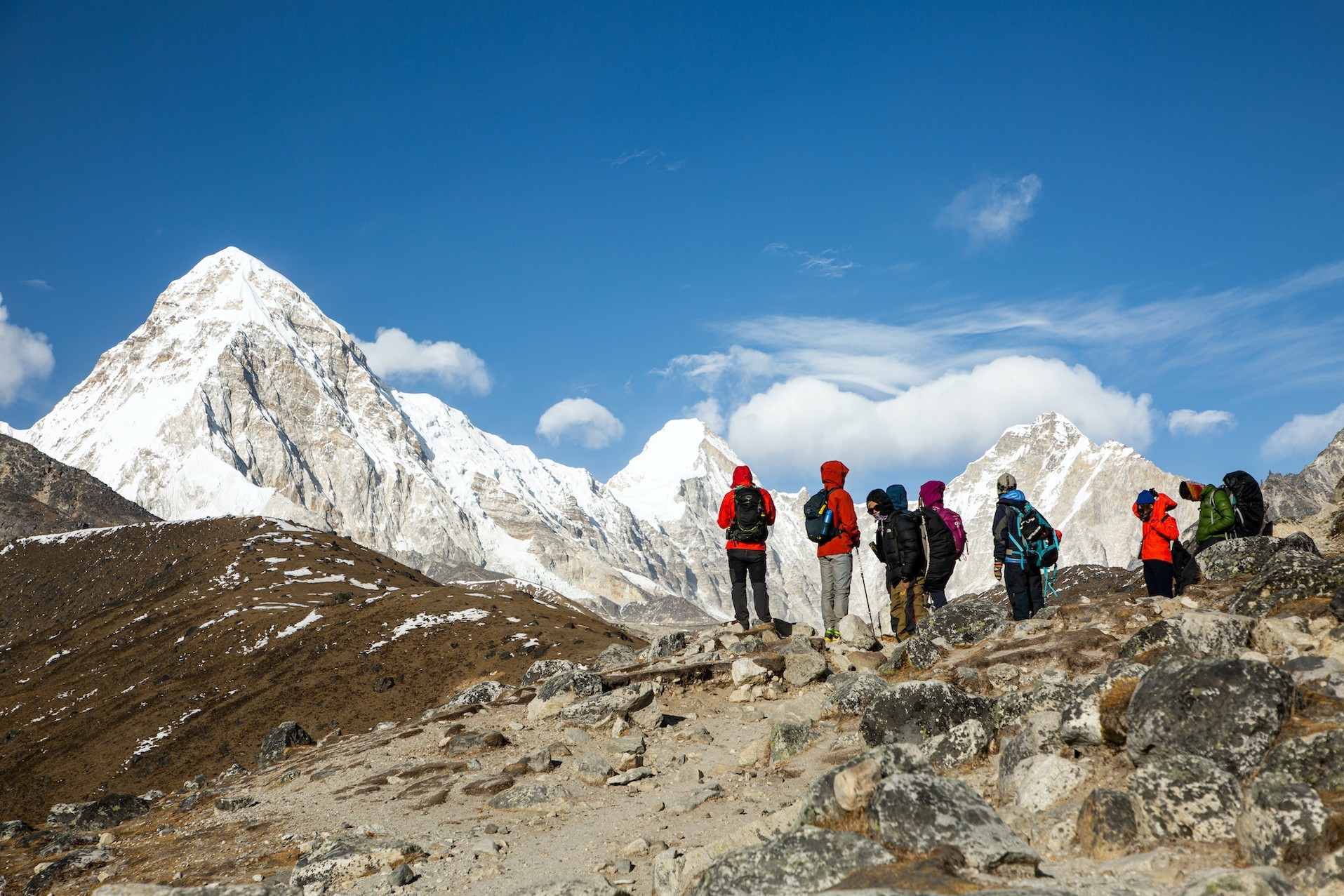 Trekkers hiking toward Gorak Shep with Mount Pumori, Nuptse, and towering snow-covered Himalayan peaks under a clear blue sky on the Everest Base Camp Trek.