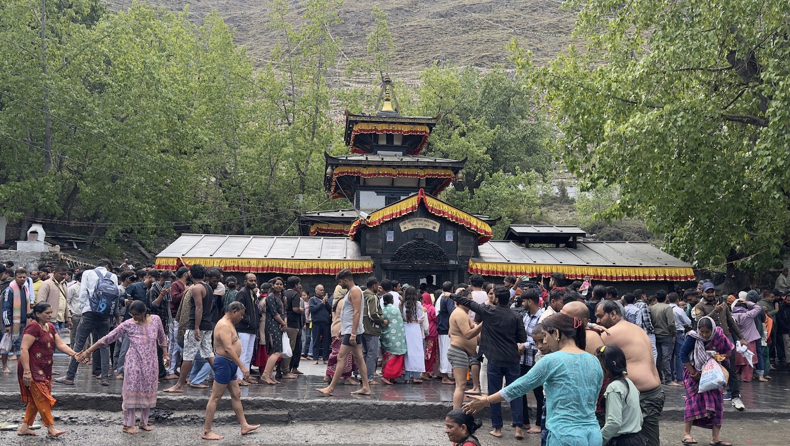 Pilgrims at Muktinath Temple performing ritual bathing under the sacred water spouts, with temple architecture, prayer flags, and Himalayan mountain backdrop.