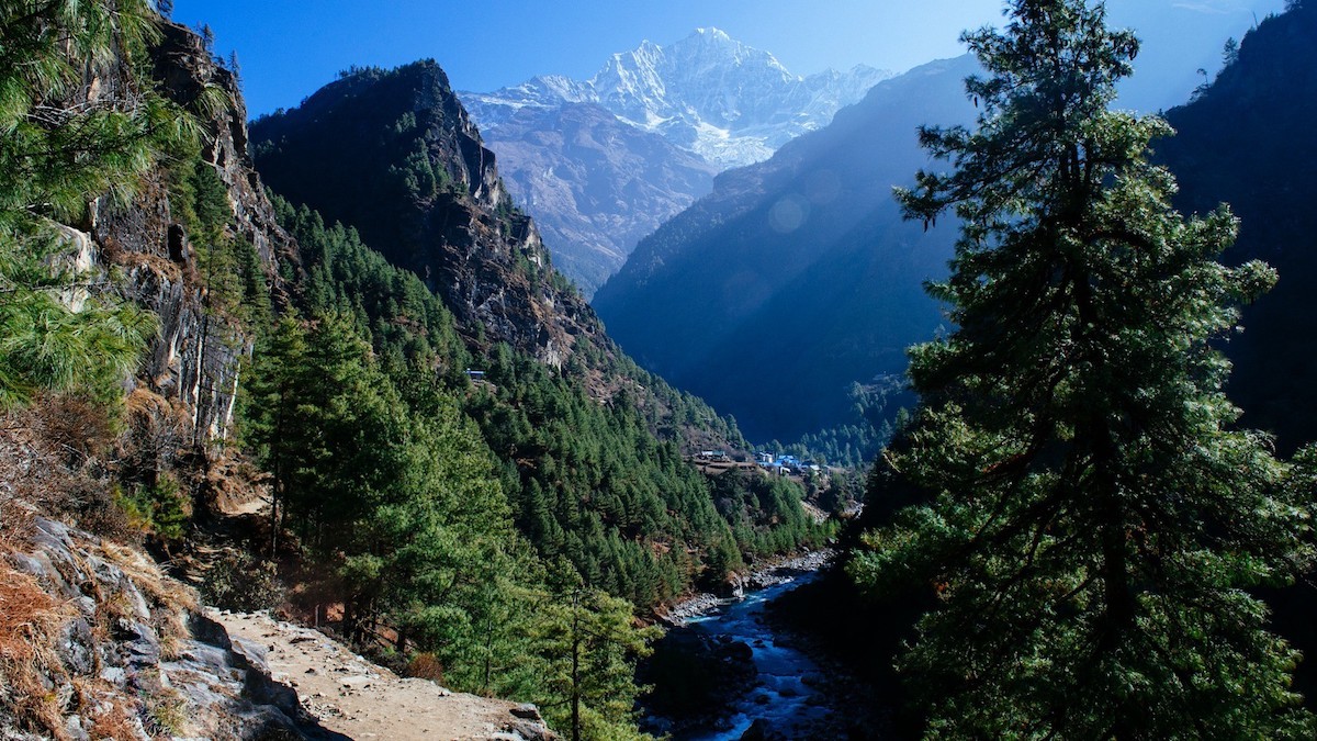 "Everest Base Camp trekking trail winding through pine and rhododendron forests beside the Dudh Koshi River with the majestic Thamserku peak rising above Nepal's Khumbu Valley