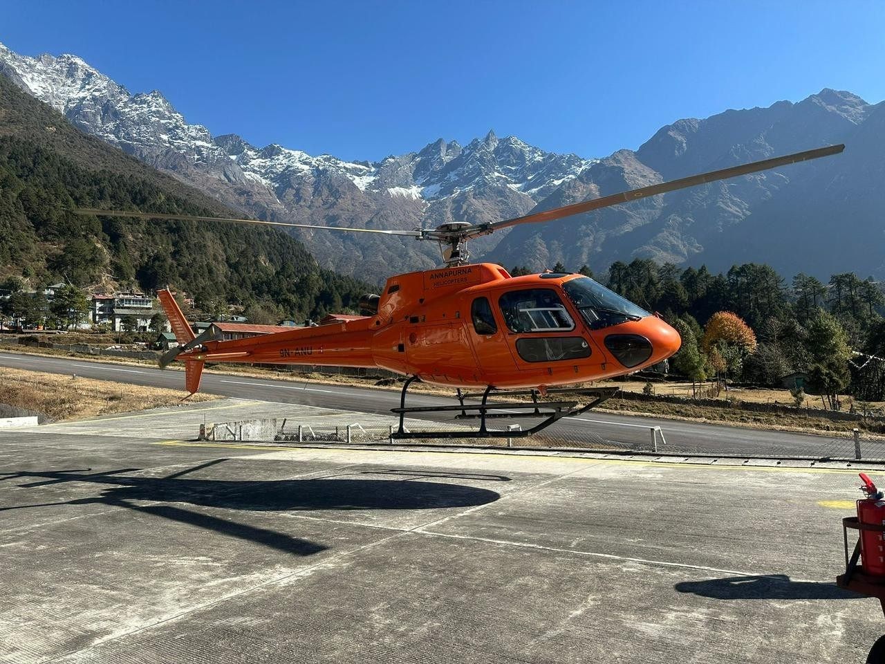 Helicopter at Lukla Airport with snow-capped Himalayan mountains in the background.