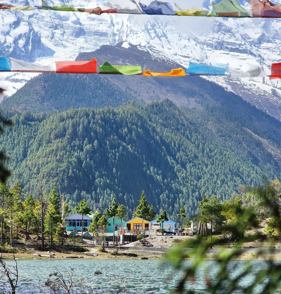 Spectacular Himalayan landscape in October with crystal-clear blue skies, lush green lower valleys, colorful forests, and snow-capped mountain peaks.