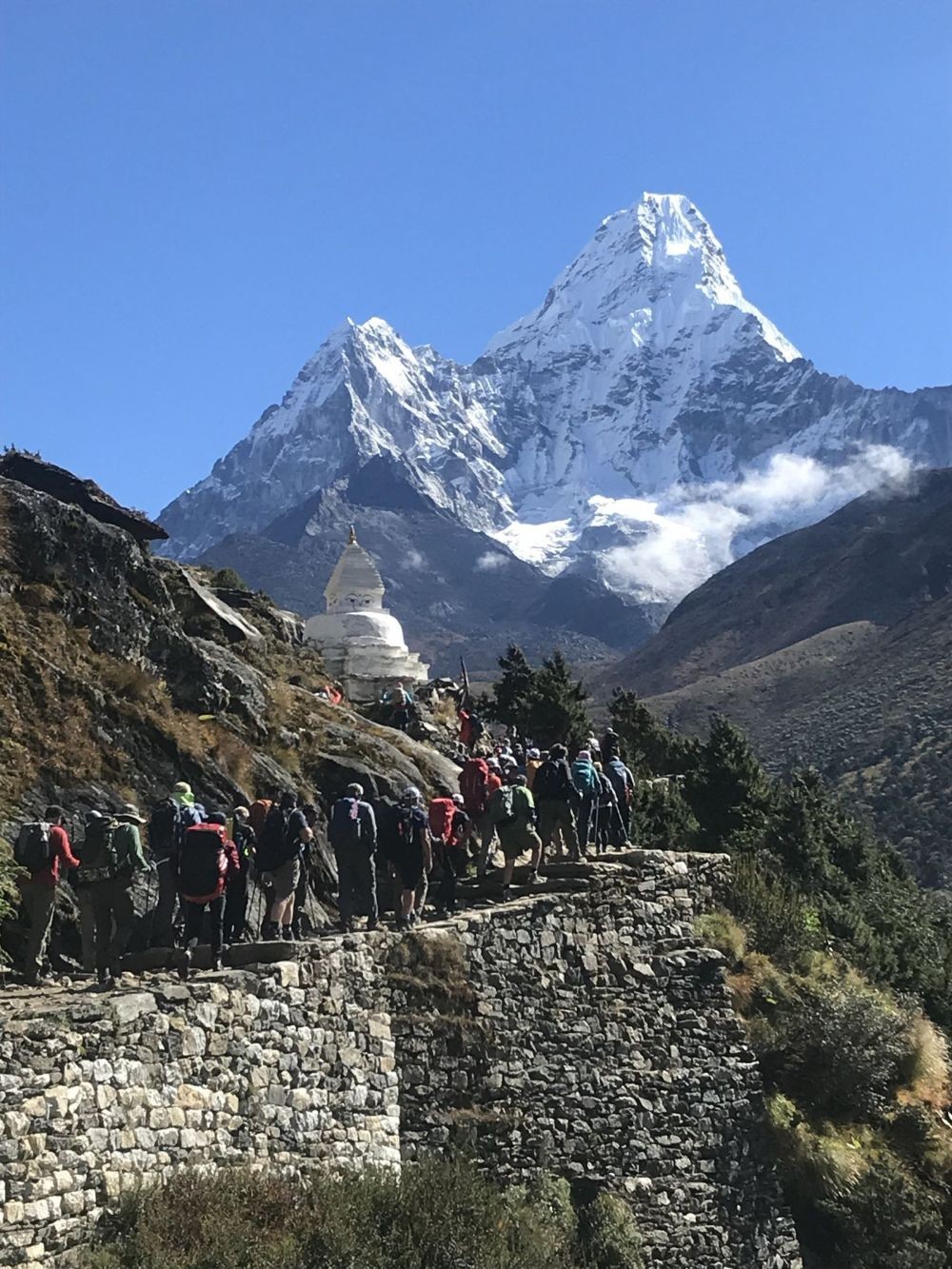 Trekkers hike along the alpine trail from Namche Bazaar to Dingboche with the iconic peak of Ama Dablam rising majestically above the Khumbu Valley beneath clear Himalayan skies.