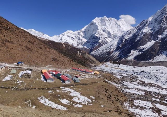 High-altitude lodge settlement at Dharmasala near Larke Pass, featuring simple mountain teahouses surrounded by barren alpine terrain and snow-capped Himalayan peaks.